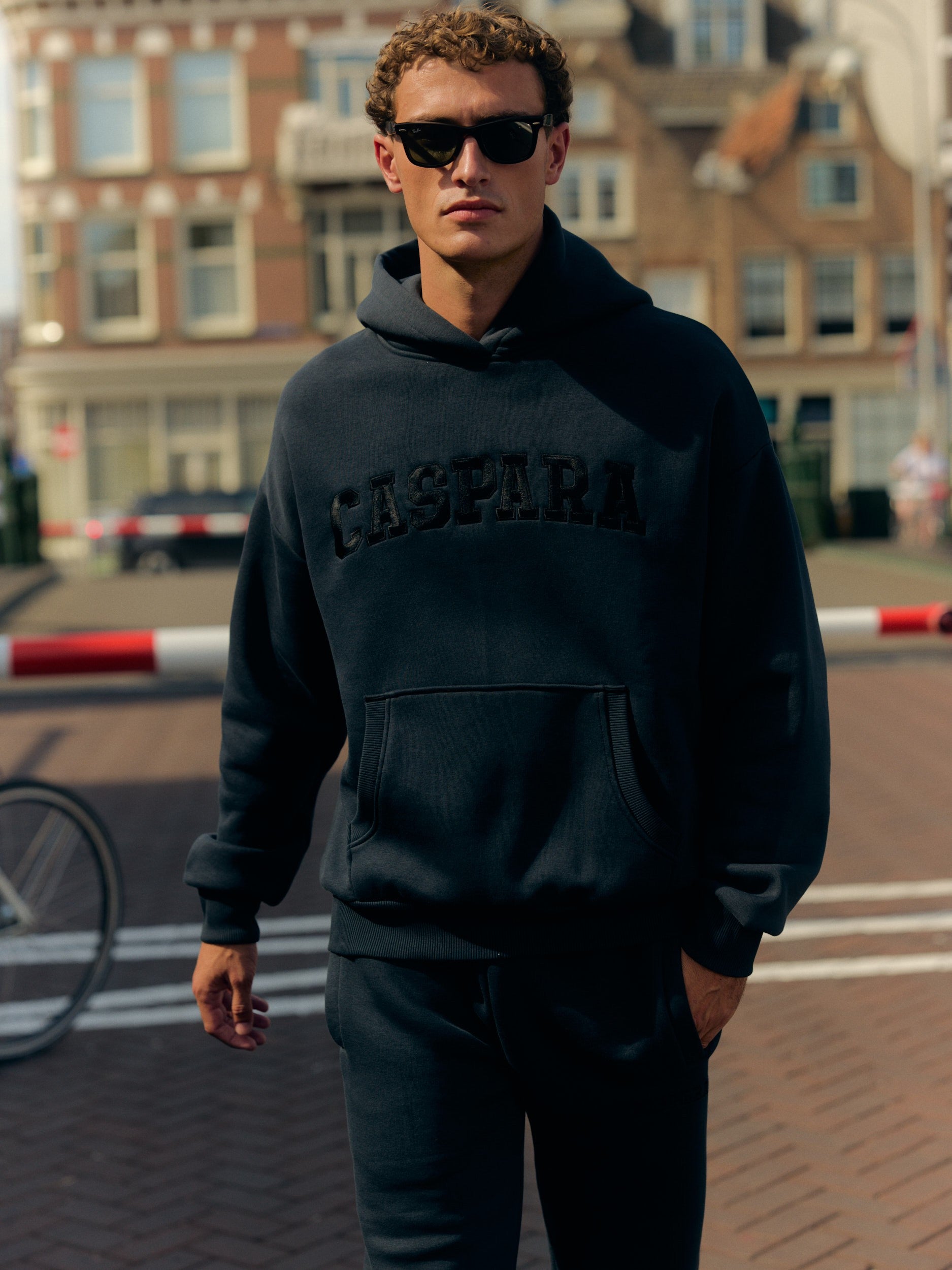 Man wearing a navy CASPARA hoodie and matching sweatpants with sunglasses on a city street.
